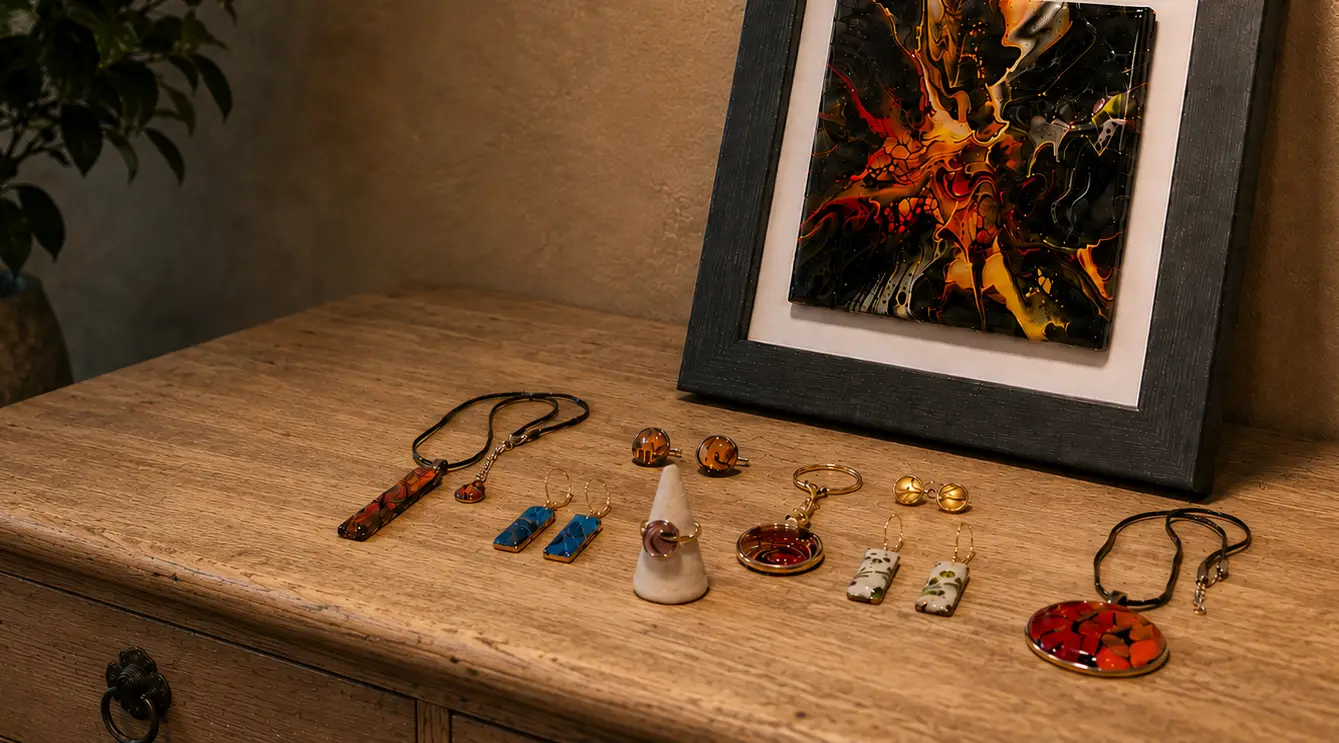 A dresser top laid with Wild Shore fluid art pendants, earrings, cufflinks, a ring and a keyring beside a framed fluid art piece