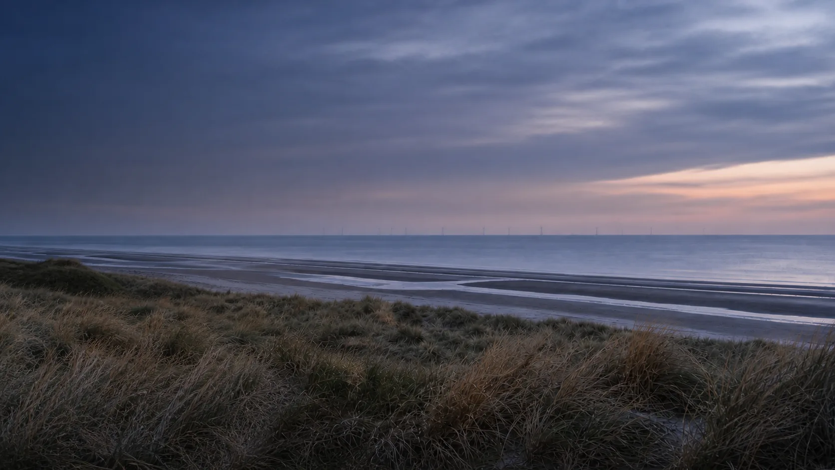 Marram dunes overlooking the Wild Shore at blue hour with a distant offshore wind farm